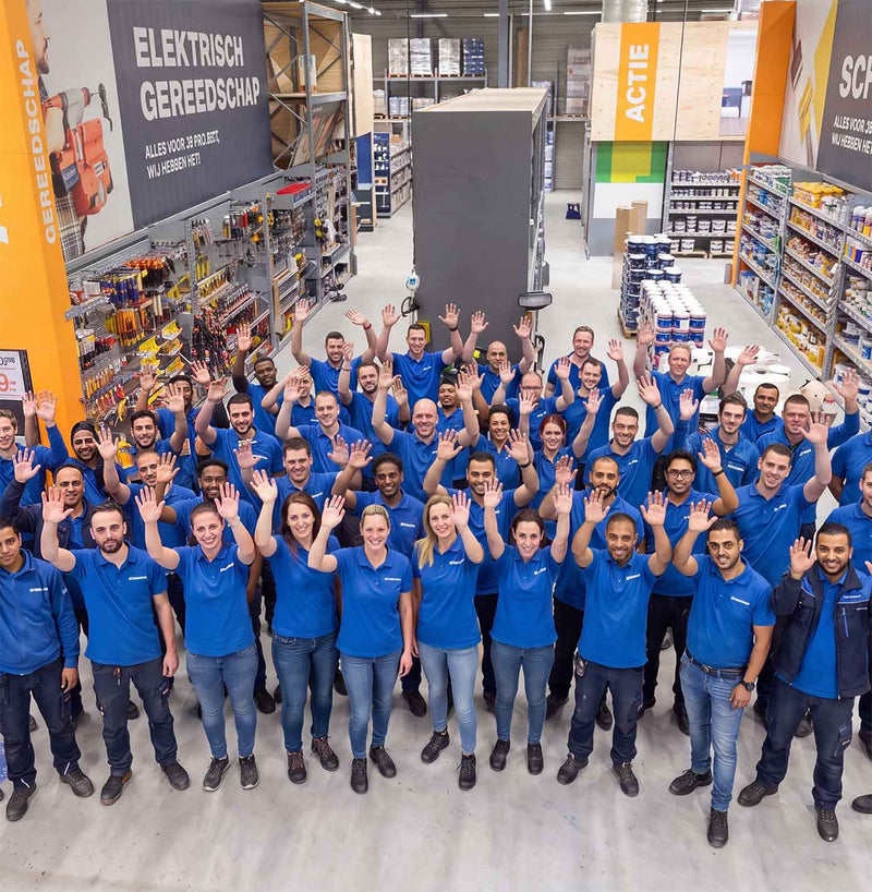 Bouwmaat medewerkers in een vestiging. Foto van bovenaf genomen, medewerkers staan met armen in de lucht.