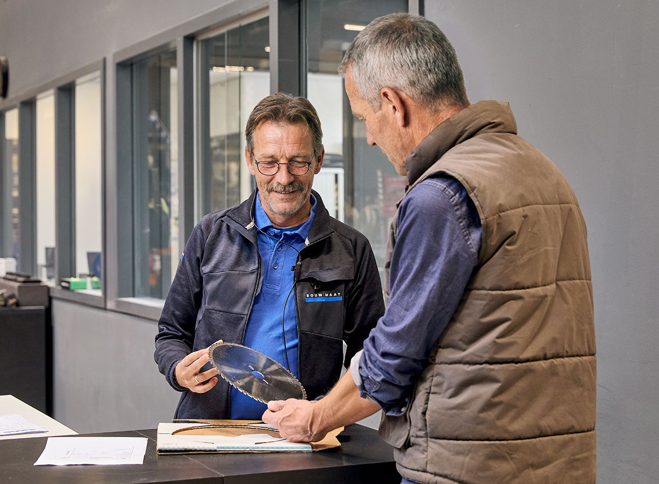 medewerker toont zaagblad aan vakman bij werkbank
 - article 1