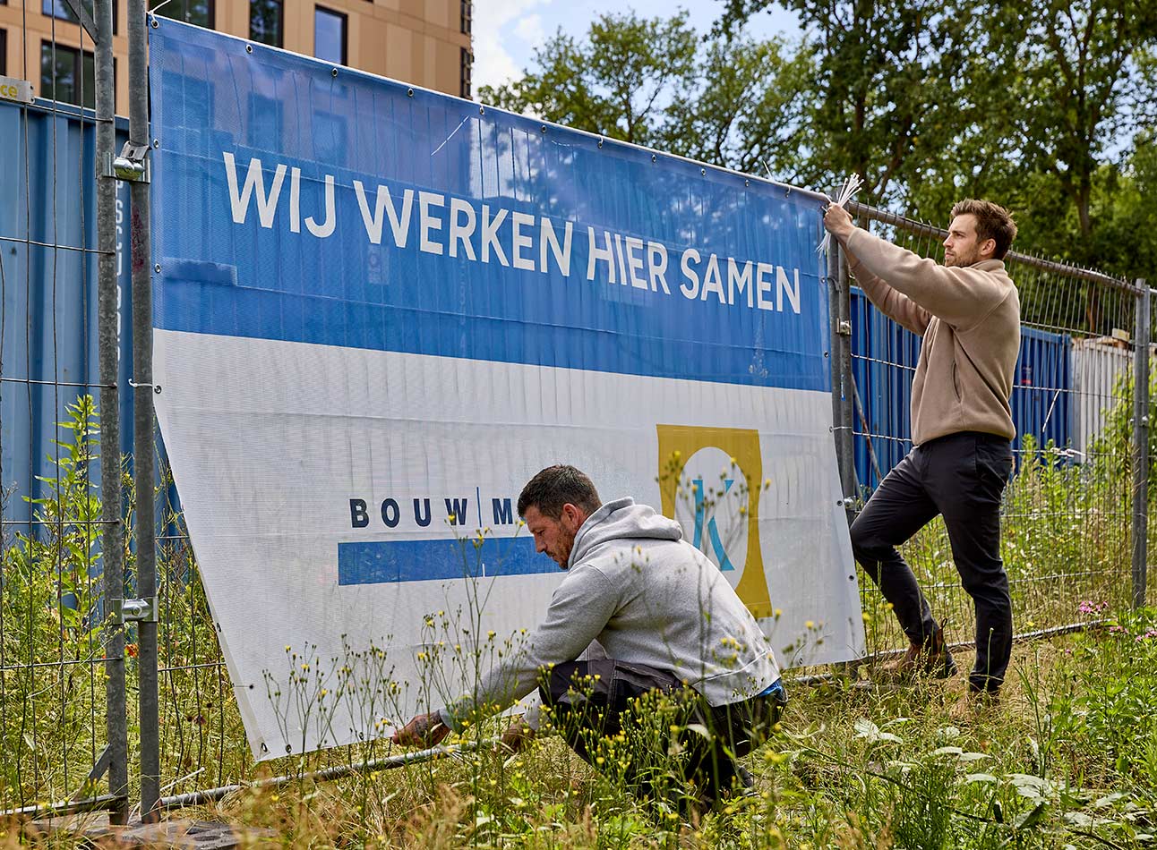 vakmannen bevestigen spandoek aan hekwerk op bouwplaats
 - article 1