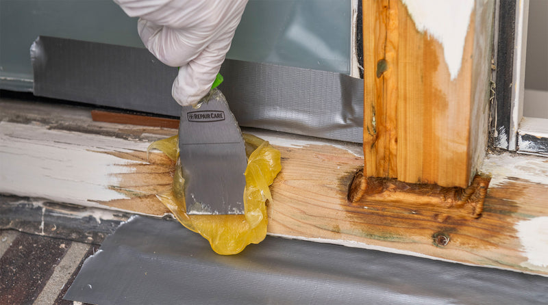 Beschadigd houten kozijn wordt gerepareerd met vulmiddel en een plamuurmes als voorbehandeling voor schilderwerk.