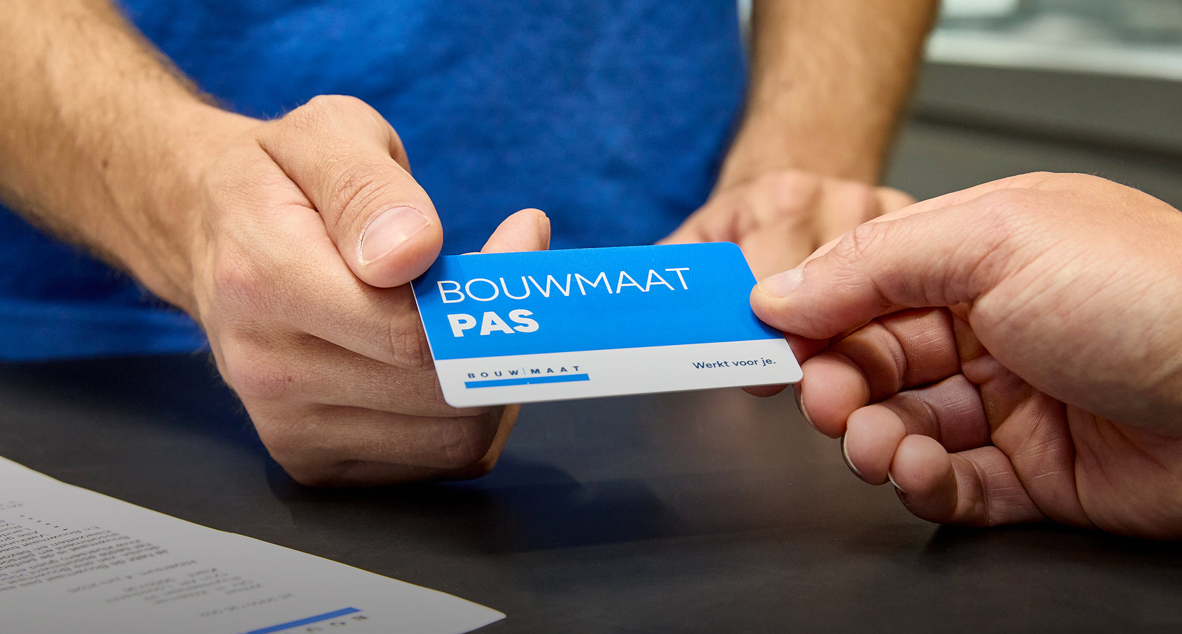 Medewerker overhandigt een Bouwmaat Pas aan een klant aan de balie