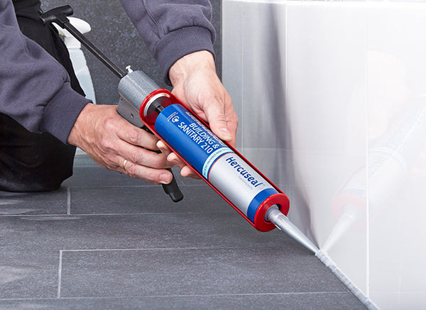 Vakman brengt sanitairkit aan langs een tegelwand voor een waterdichte badkamerafwerking - card 1